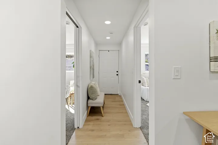 Bright hallway featuring recessed ceiling lighting, wood-finish flooring, and clean white walls with multiple doorway openings