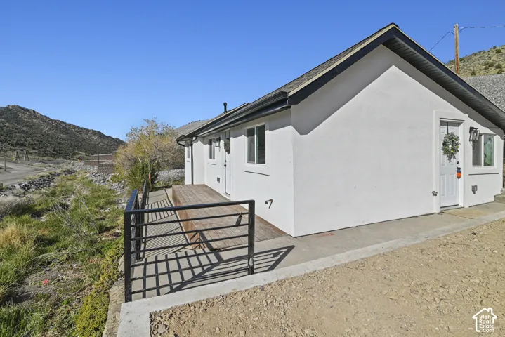 Exterior featuring white stucco finish, dark roof shingles, and a wood-finish deck with a black metal railing