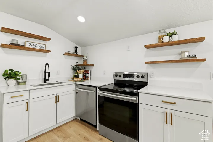 Modern kitchen featuring white cabinetry with brass hardware, stainless steel appliances including a convection electric range, undermount sink with pull-down faucet, quartz countertops, and floating wood-finish shelving for open storage and display