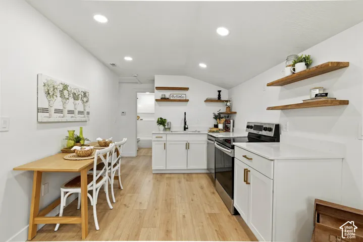 Modern kitchen featuring white cabinetry, stainless steel appliances, wood-finish flooring, and floating wood shelving