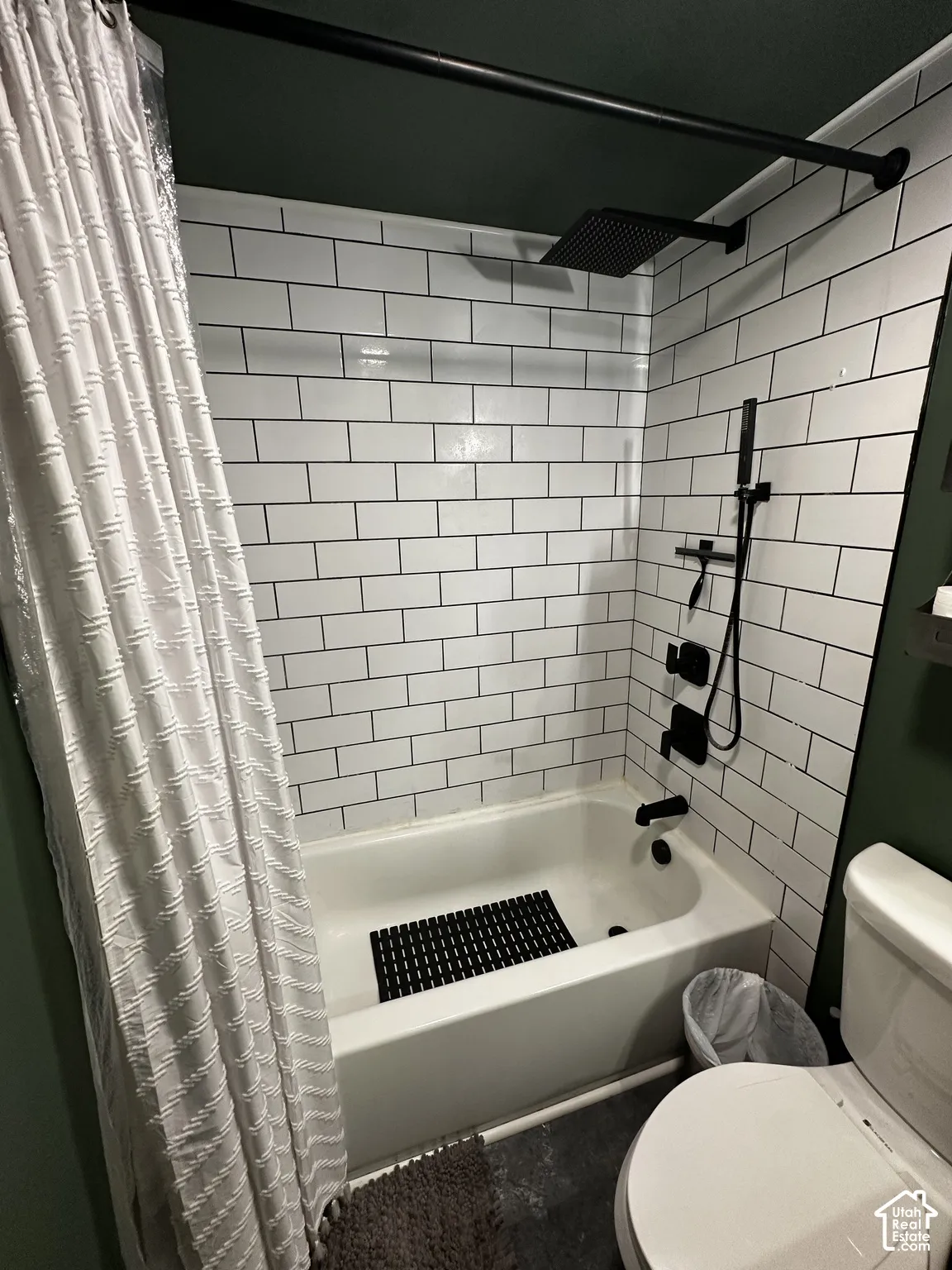 Bathtub surround featuring white subway tile, matte black rain-style shower head, adjustable handheld shower wand, and matching matte black plumbing fixtures