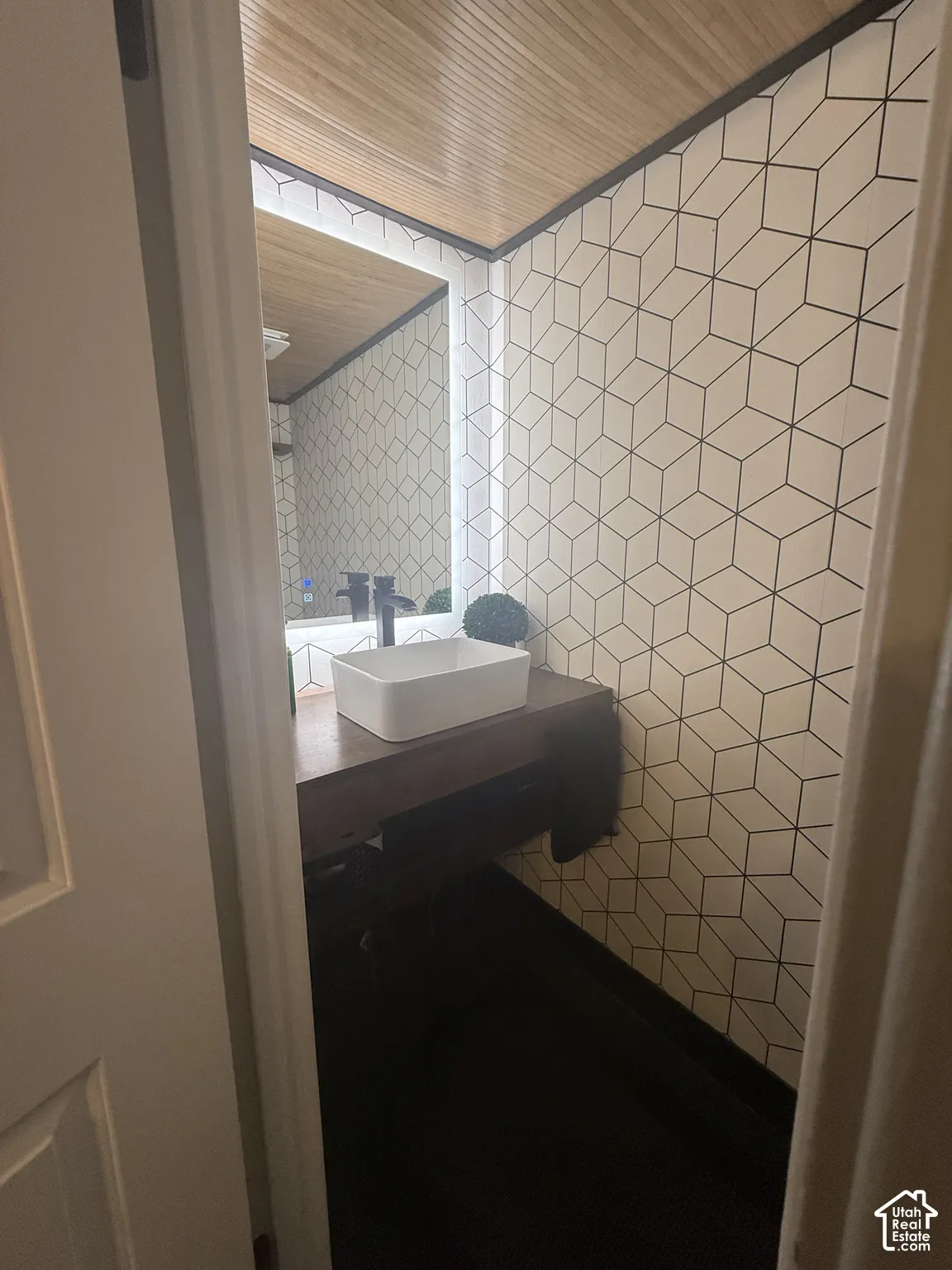 Geometric patterned tile walls, wood-slat ceiling, dark wood-finish vanity, rectangular vessel sink, and integrated LED-backlit mirror
