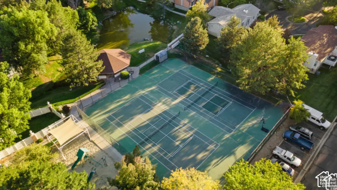 Community recreation area featuring dual tennis courts, a gazebo, and a shaded playground area surrounded by mature trees and water frontage