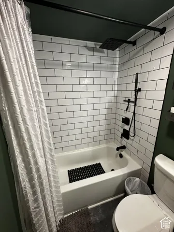 Bathtub surround featuring white subway tile, matte black rain-style shower head, adjustable handheld shower wand, and matching matte black plumbing fixtures