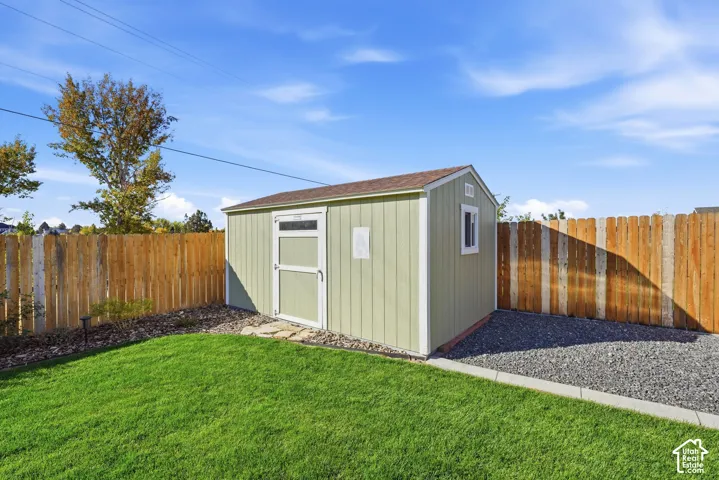 Manicured lawn with a gravel area, wood privacy fence, and a storage shed with a shingle roof and a functional window