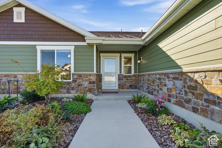 Exterior featuring a stone and siding facade, a covered entry, established landscaping, and a concrete pathway