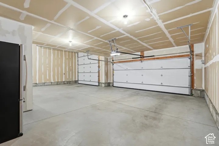 Two white overhead garage doors, concrete flooring, exposed drywall, and overhead lighting