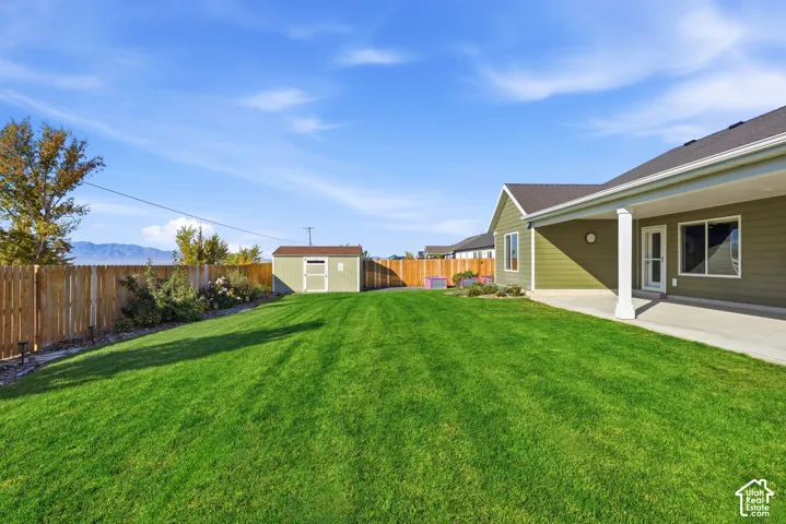 Expansive green lawn, wood fence perimeter, covered concrete patio, exterior storage shed, and a mountain backdrop