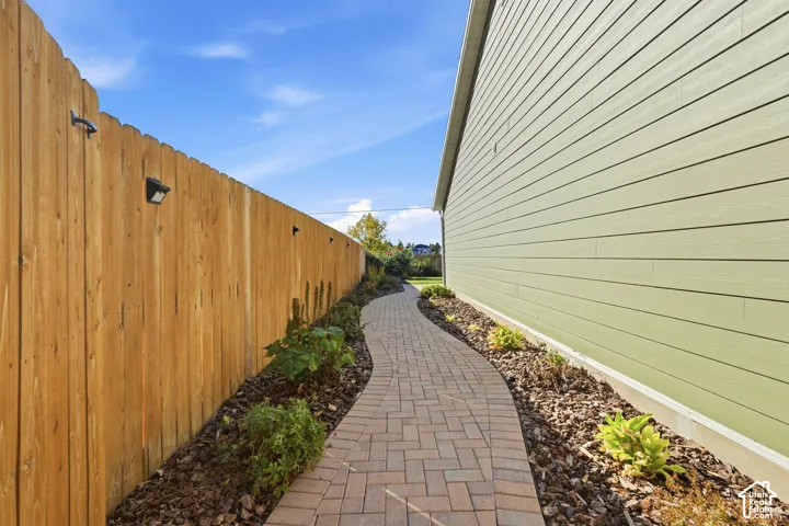 Paver pathway bordered by landscaping and a wood fence with exterior lighting