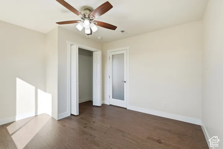 Wood-finish flooring, ceiling fan with integrated lighting, white interior door with frosted glass panel, and bi-fold closet doors