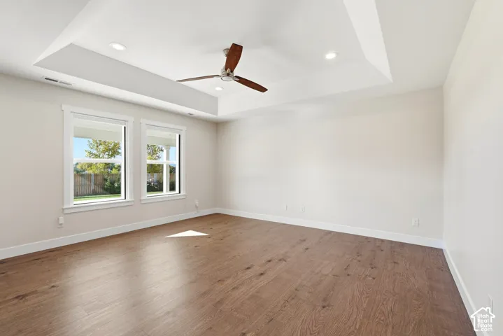 Tray ceiling with recessed lighting and a ceiling fan, wood-finish flooring, and dual windows