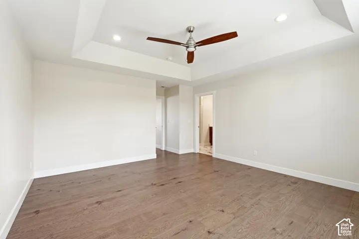 Tray ceiling with recessed lighting, wood-finish flooring, and a ceiling fan
