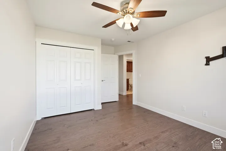 Wood-finish flooring, white walls, bi-fold closet doors, and an overhead ceiling fan