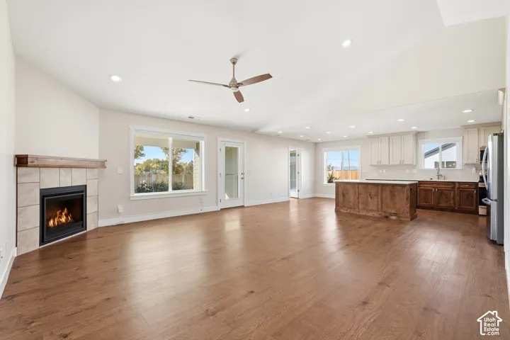 Open-concept living area with wood-finish flooring, a corner fireplace with a wood mantle, and a ceiling fan