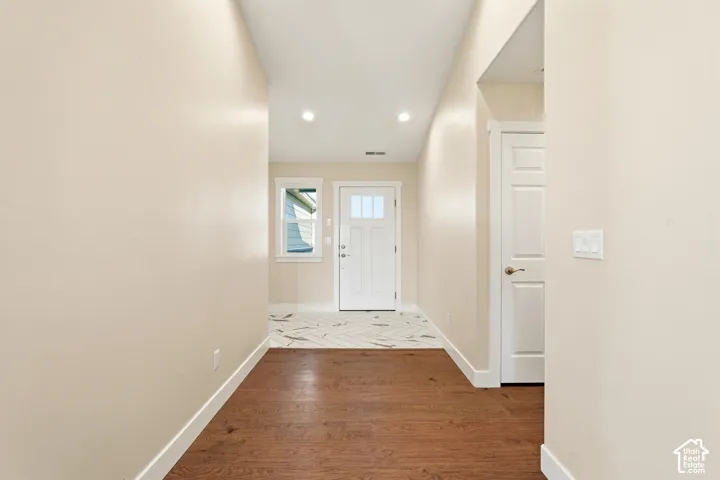 Wood-finish flooring leading to a tiled entry, featuring a white paneled door with glass inserts, and a single window with white trim