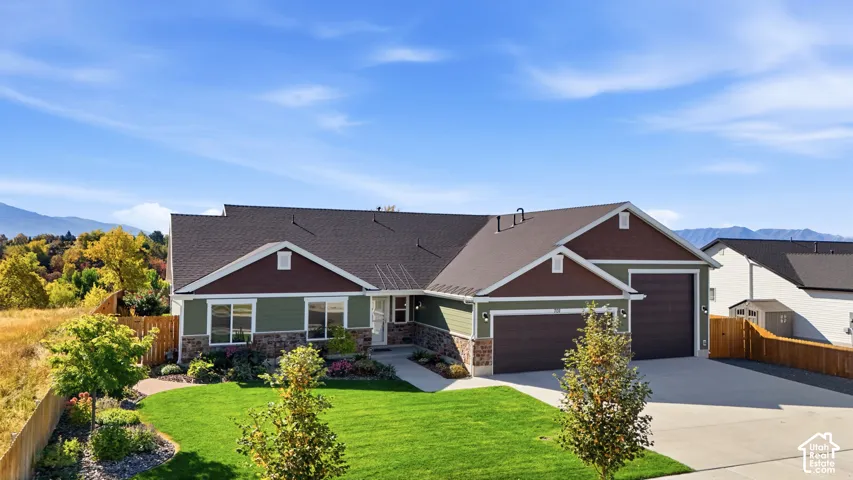 Contemporary residence featuring a two-car garage, stone and siding exterior, manicured lawn, concrete driveway, and a mountain backdrop