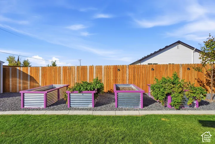 Manicured lawn with a concrete walkway, four raised garden beds with metal and wood-finish construction, and a wood-panel fence