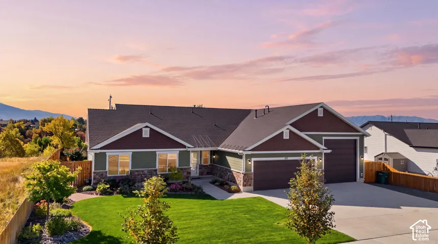 Contemporary ranch home featuring a dual-tone exterior, stone accents, two-car garage, manicured lawn, and mature trees