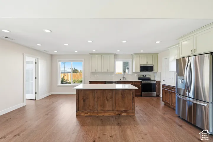 Open-concept kitchen featuring wood-finish flooring, recessed lighting, a central island with a solid surface countertop, stainless steel appliances, and white shaker-style upper cabinetry