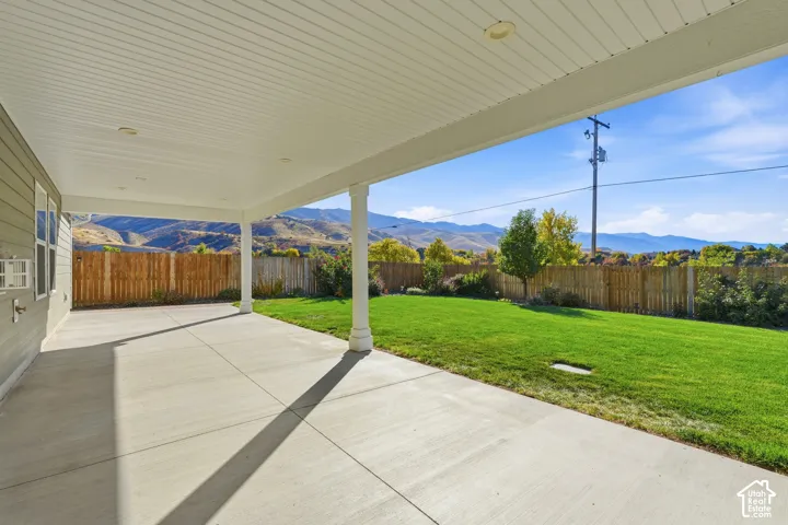 Covered concrete patio with recessed lighting, verdant lawn, and wood privacy fencing