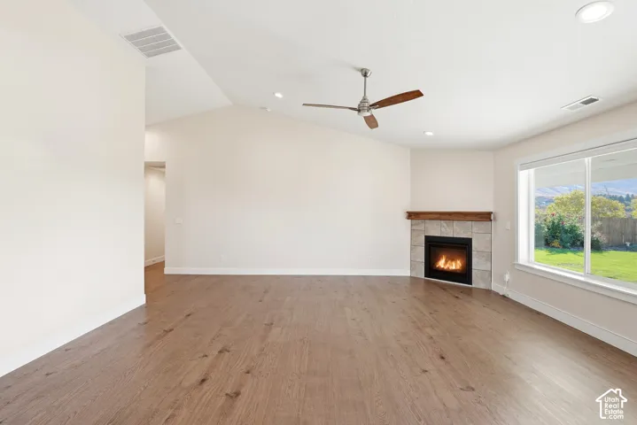 Wood-finish flooring, vaulted ceiling, and a corner fireplace with a wood mantle and stone surround