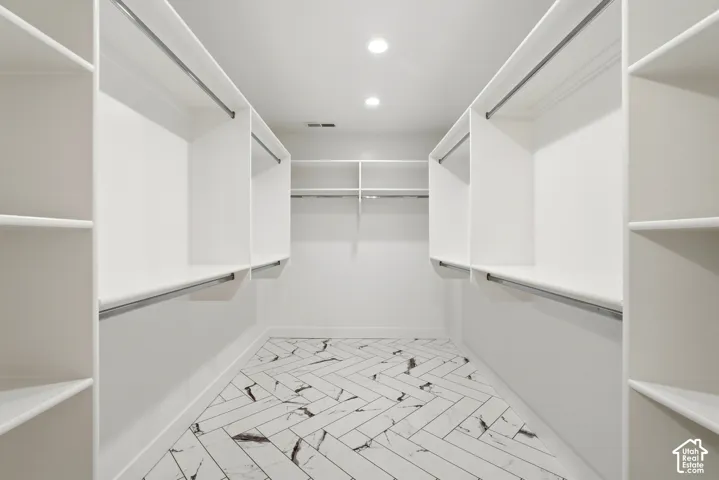 Recessed lighting illuminates extensive built-in shelving, hanging rods, and a herringbone-patterned tile floor