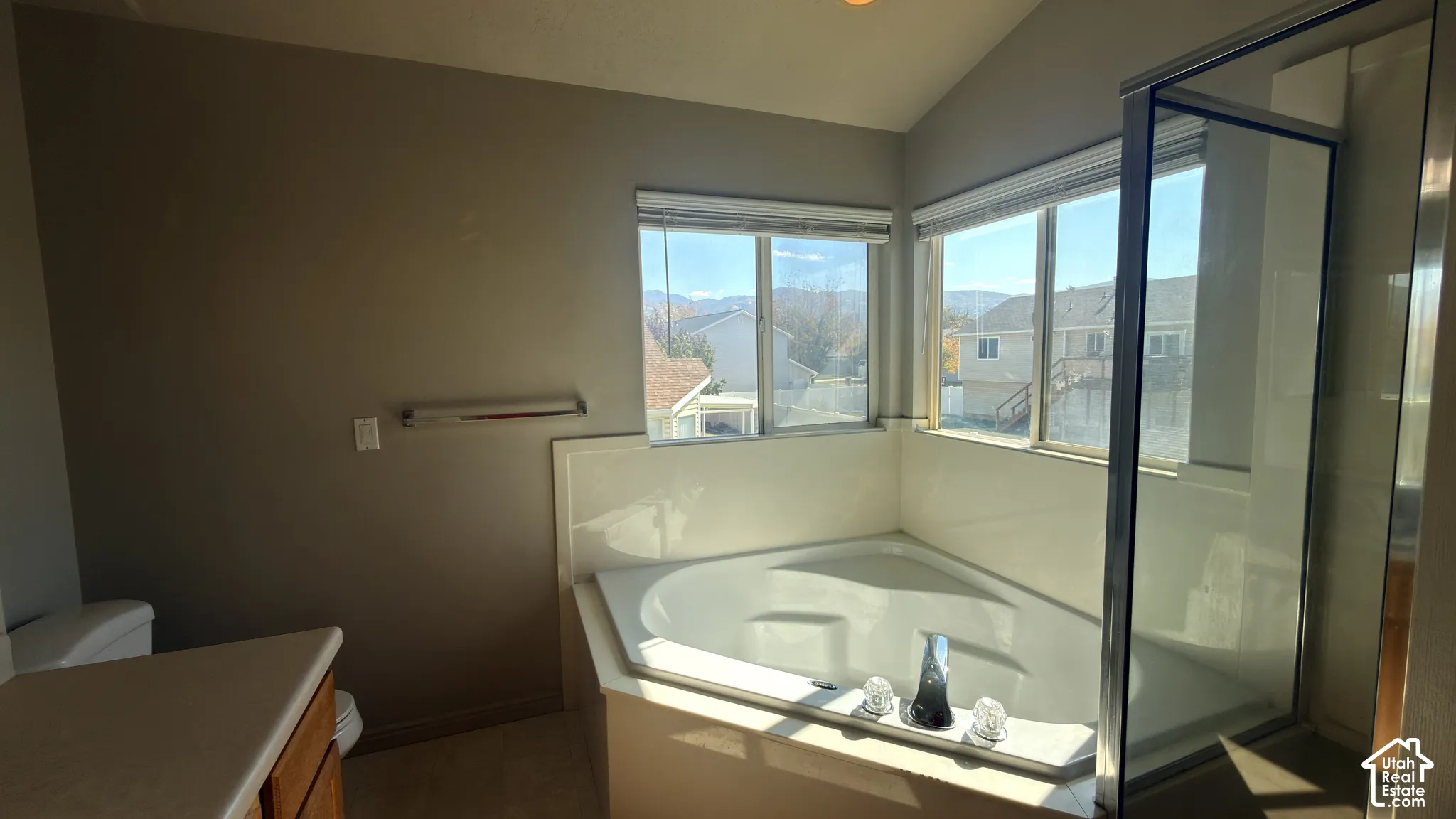 Corner soaking tub with surrounding windows, glass-enclosed shower, and wood-finish vanity
