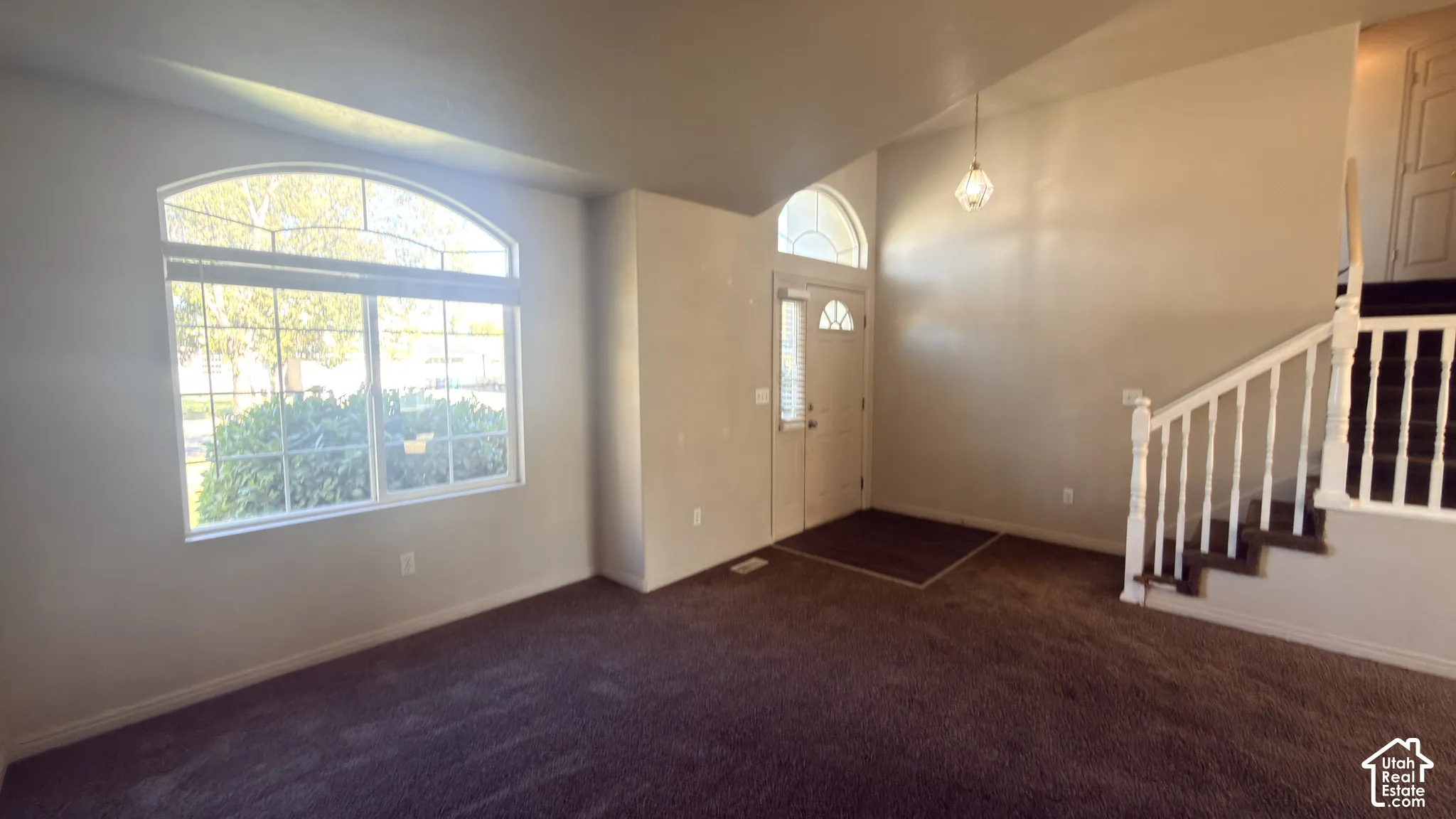 Arched transom window, vaulted ceiling, white spindle staircase, entryway door with decorative glass, and a hanging pendant light fixture
