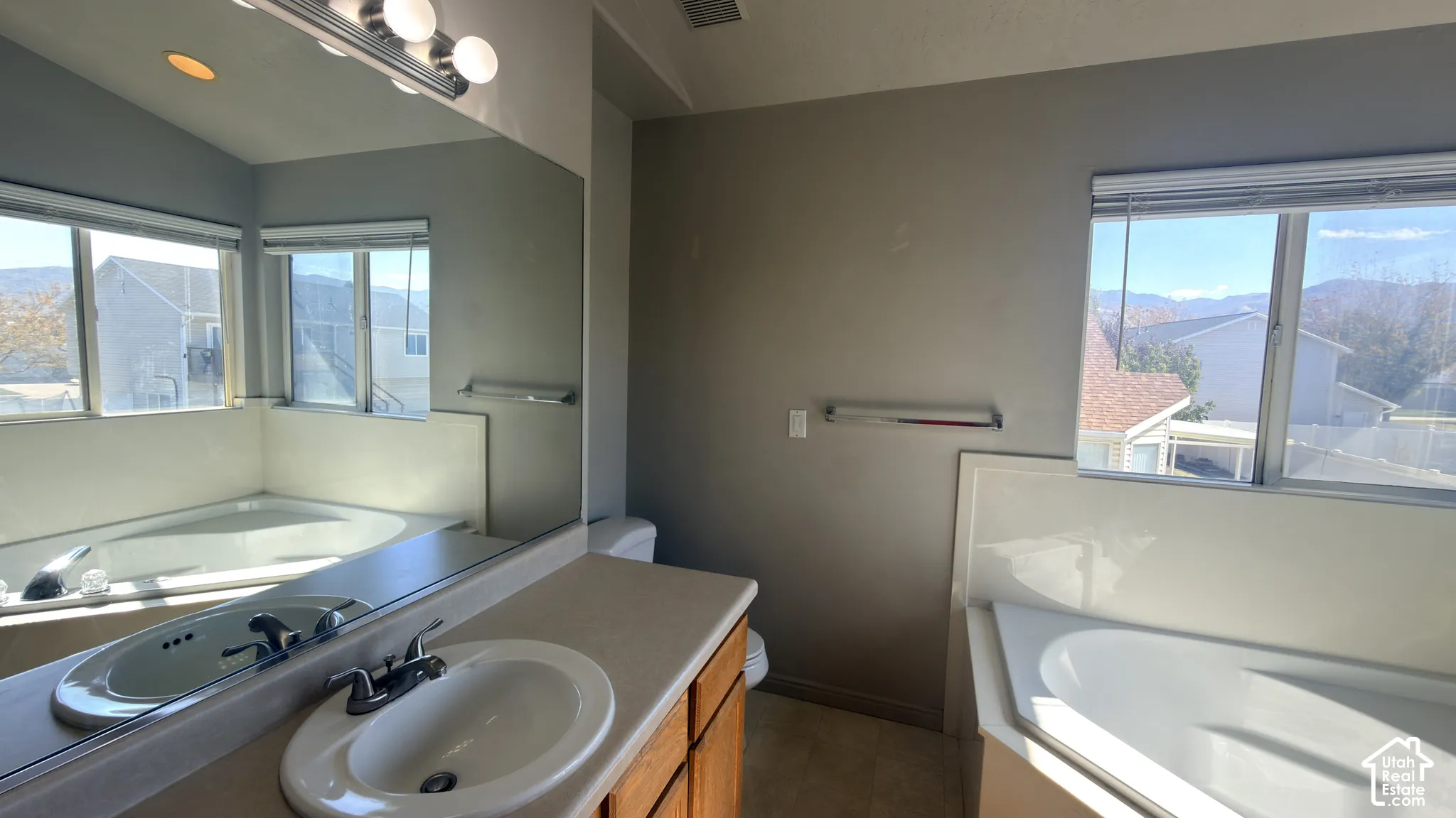 Bathroom featuring a large corner soaking tub, a vanity with a drop-in sink, and multiple windows