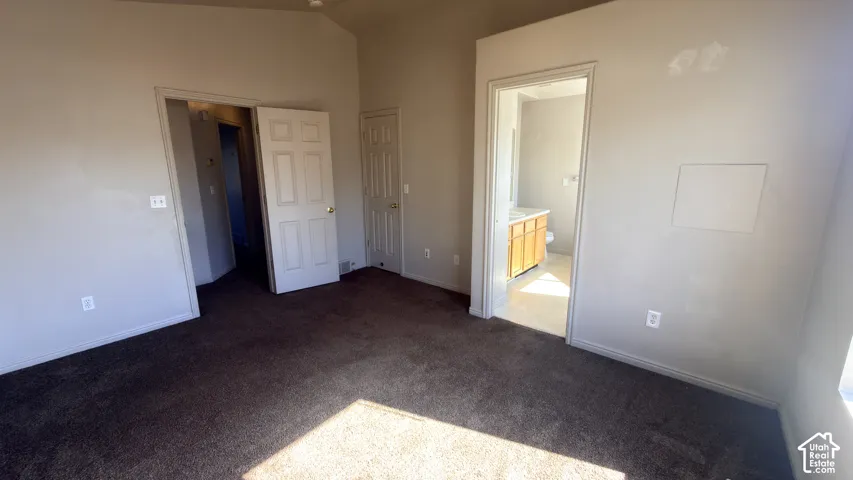 Vaulted ceiling, wall-to-wall carpeting, and a visible doorway to a bathroom featuring a wooden vanity