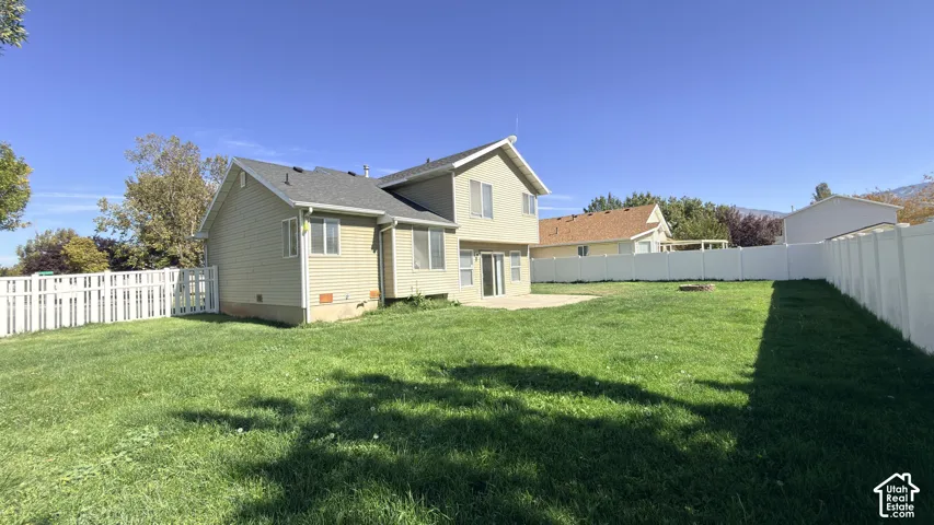 Expansive green space featuring a concrete patio, fully fenced perimeter, and vinyl siding exterior