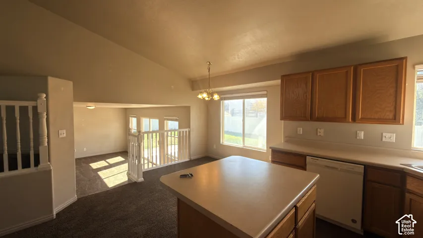 Vaulted ceilings, kitchen island with counter seating, wood cabinetry, built-in dishwasher, and multiple windows