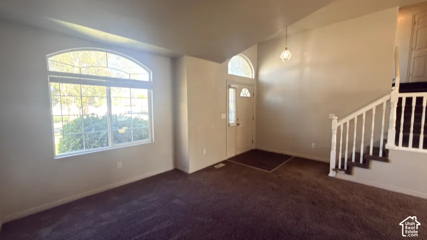 Arched transom window, vaulted ceiling, white spindle staircase, entryway door with decorative glass, and a hanging pendant light fixture