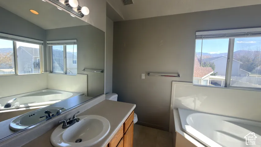 Bathroom featuring a large corner soaking tub, a vanity with a drop-in sink, and multiple windows