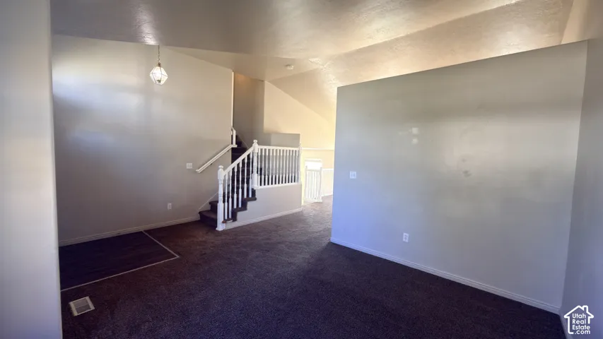 Carpeted flooring, vaulted ceiling, and a staircase with white spindles and handrail