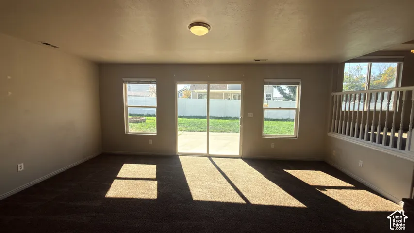 Open-concept living space with dark brown carpeting, neutral wall tones, and a sliding glass door providing outdoor access to a concrete patio and grass yard