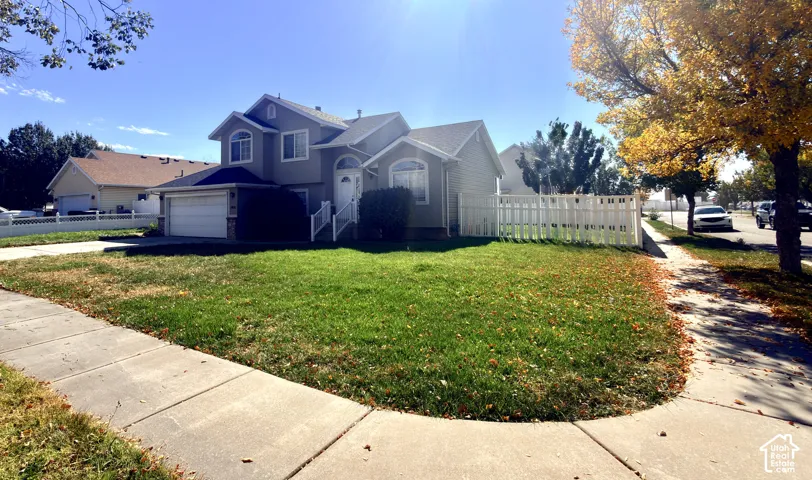 Two-story exterior featuring beige siding, an attached two-car garage, and white vinyl perimeter fencing