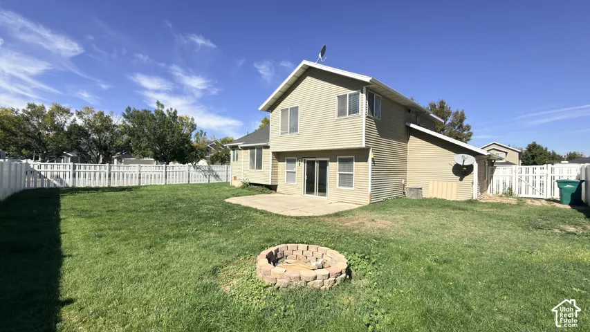 Expansive backyard with a manicured lawn, full perimeter fencing, and a built-in stone fire pit