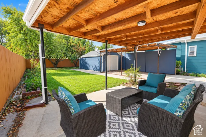 Covered patio featuring an exposed timber-beam ceiling, concrete slab flooring, wood-panel fencing, and a detached garage