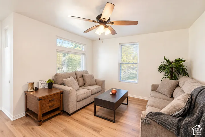 Living area featuring wood-finish flooring, a multi-blade ceiling fan with integrated lighting, and multiple windows providing natural light