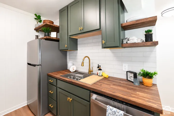Olive-toned shaker cabinetry with brass hardware, wood-finish countertops, white subway tile backsplash, floating wood shelves, and a gooseneck faucet