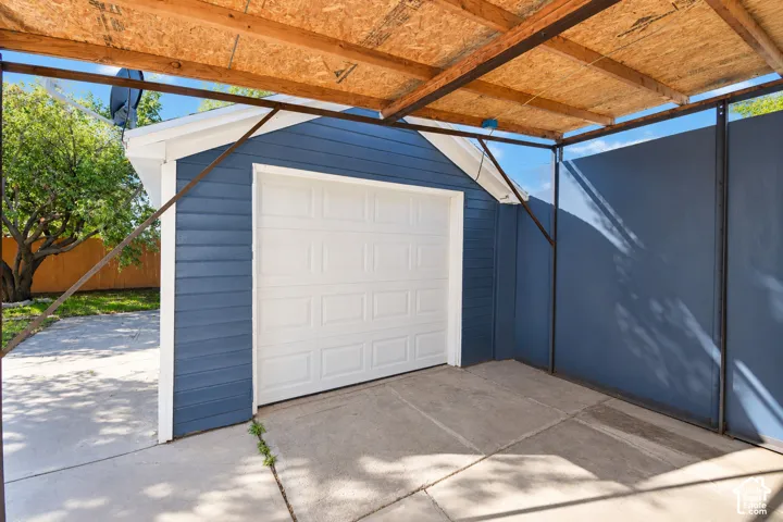 Detached garage with lap siding, sectional overhead door, and an attached metal-framed covered parking area with exposed wood-sheathing roof structure