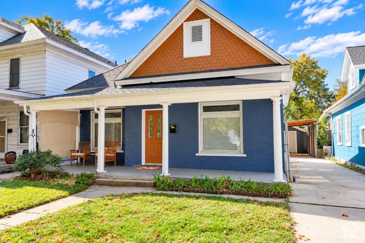 Exterior facade featuring painted brick, decorative shingle siding in the gable, a covered front porch with column supports, and a concrete driveway
