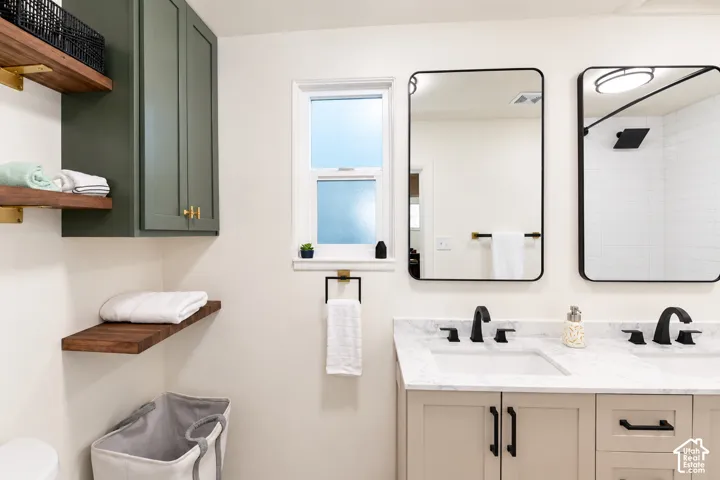 Dual-sink vanity with stone-finish countertop and matte black fixtures, custom olive-toned cabinetry, and floating wood-finish shelving