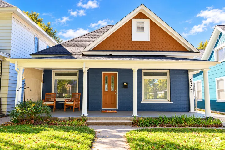 Single-story exterior featuring a brick facade, covered front porch with column supports, decorative shingle-patterned gable, and a paneled entry door with glass accents