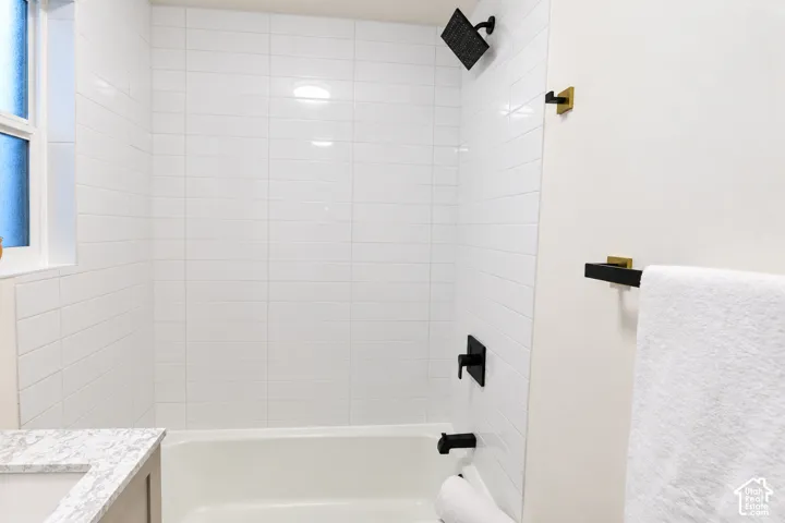 Full-height white subway tile surround, matte black rainfall shower head and faucet hardware, built-in tub, and stone-finish vanity countertop