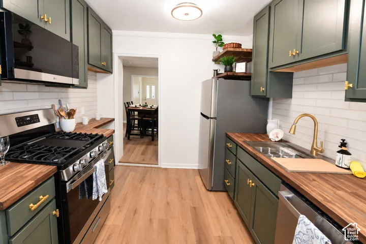 Kitchen featuring deep olive-toned cabinetry, butcher block countertops, a white subway tile backsplash, gold-finished hardware, and wood-finish flooring