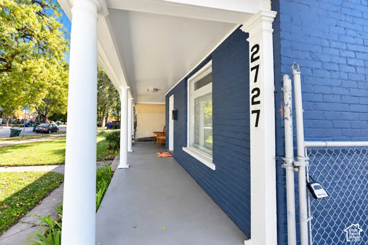 Covered front porch featuring painted brick exterior walls, classic columns, and concrete flooring
