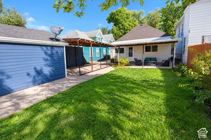 Backyard featuring a grass lawn, paved driveway, metal-framed carport, and covered concrete patio area