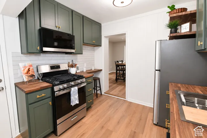 Kitchen featuring olive-toned cabinetry, wood-finish countertops, subway tile backsplash, and stainless steel appliances